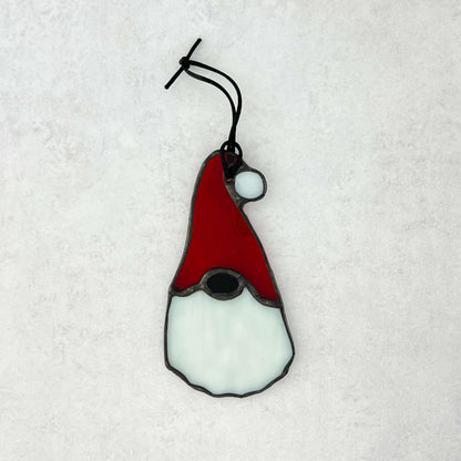 the back side of Stained glass gnome ornament with red hat and white beard on a textured white background. The hat has a white ball at the end.