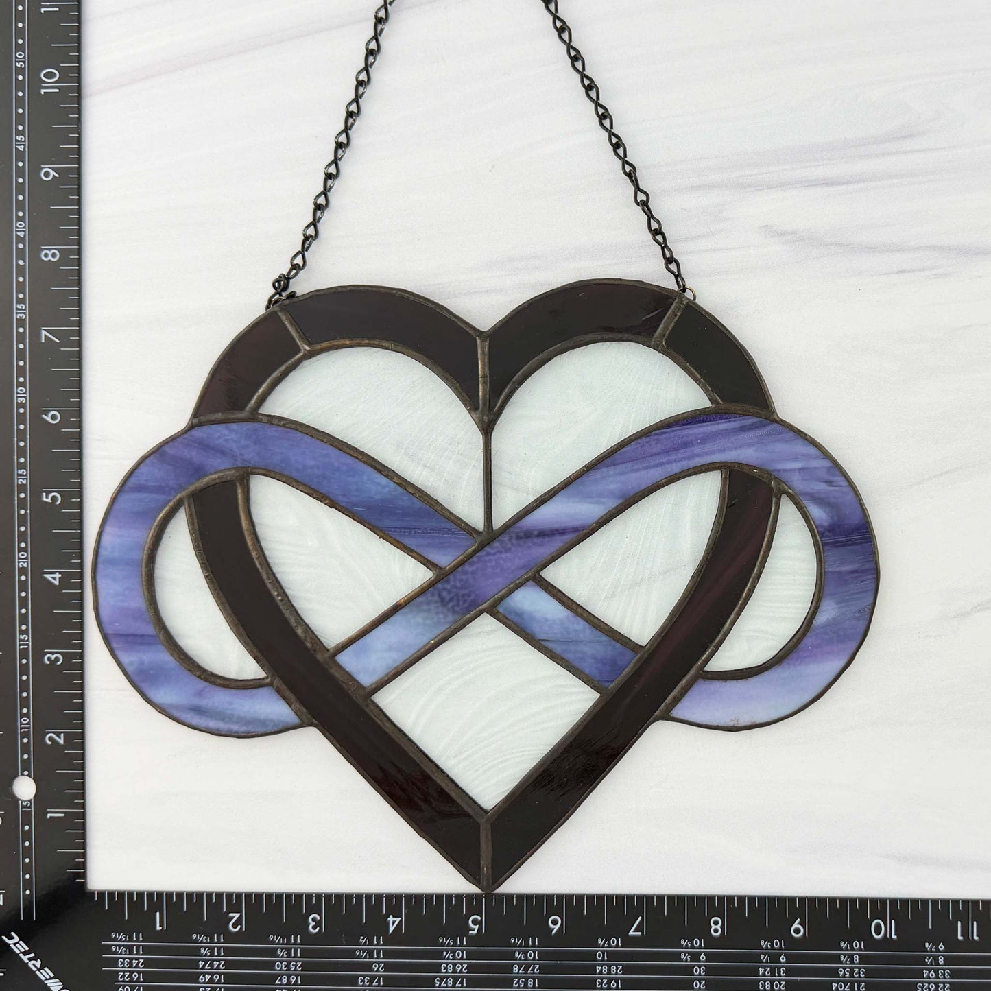 Heart-shaped stained glass piece with infinity symbol, size reference on a ruler