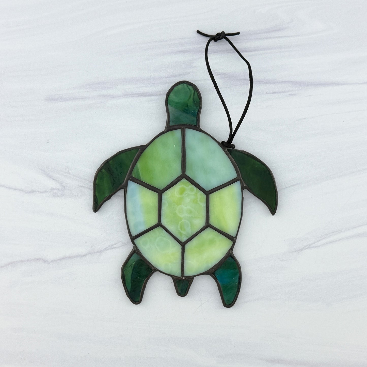 Stained glass turtle suncatcher with a shell of mottled light green opaque glass and flippers and head of translucent blue-green glass. It's displayed on a white background