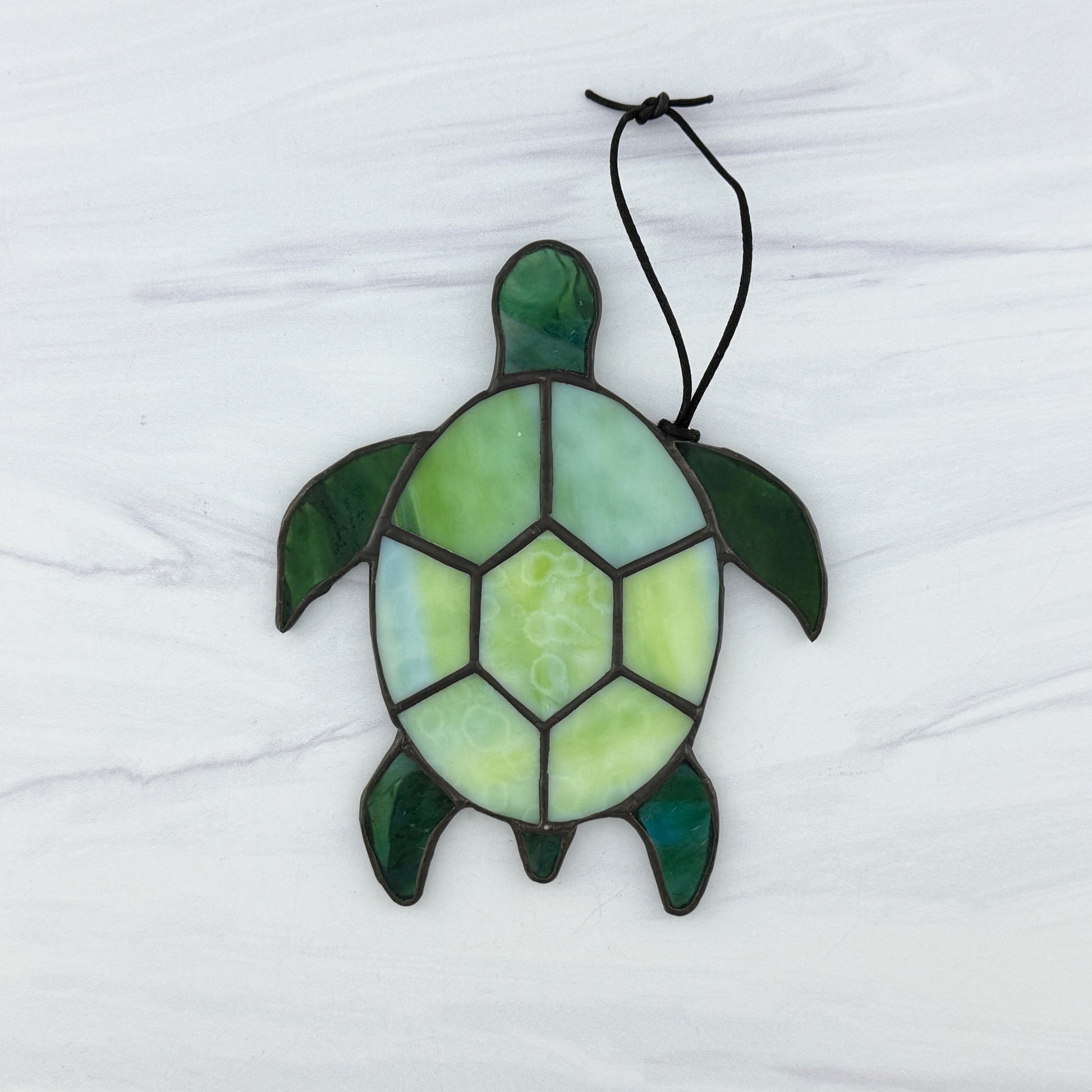 Stained glass turtle suncatcher with a shell of mottled light green opaque glass and flippers and head of translucent blue-green glass. It's displayed on a white background