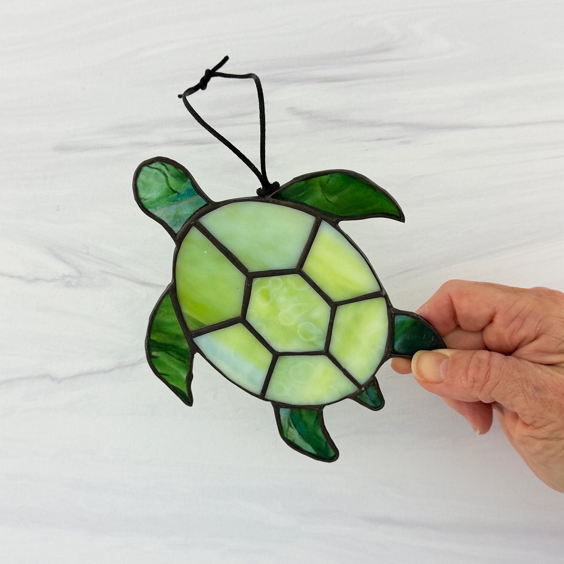 Stained glass turtle suncatcher held by a hand on a white background