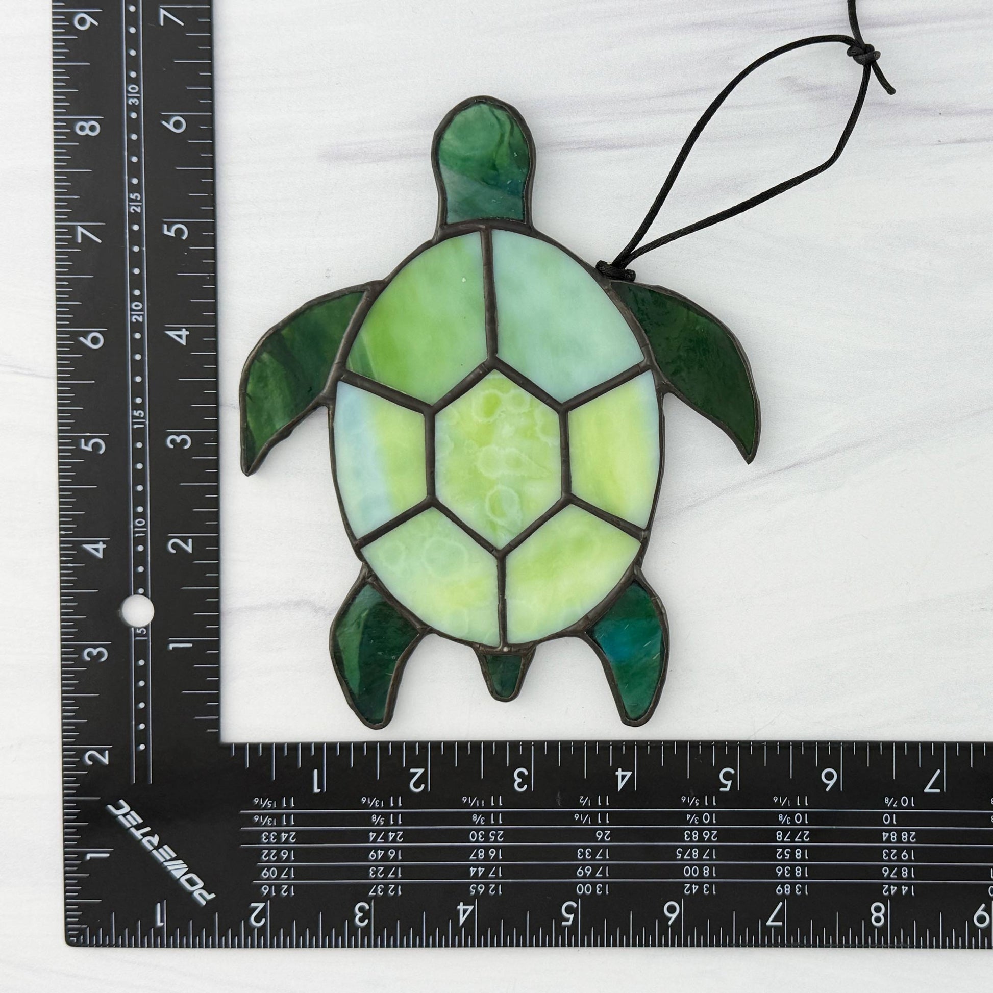 Stained glass turtle decoration next to a ruler on a white background