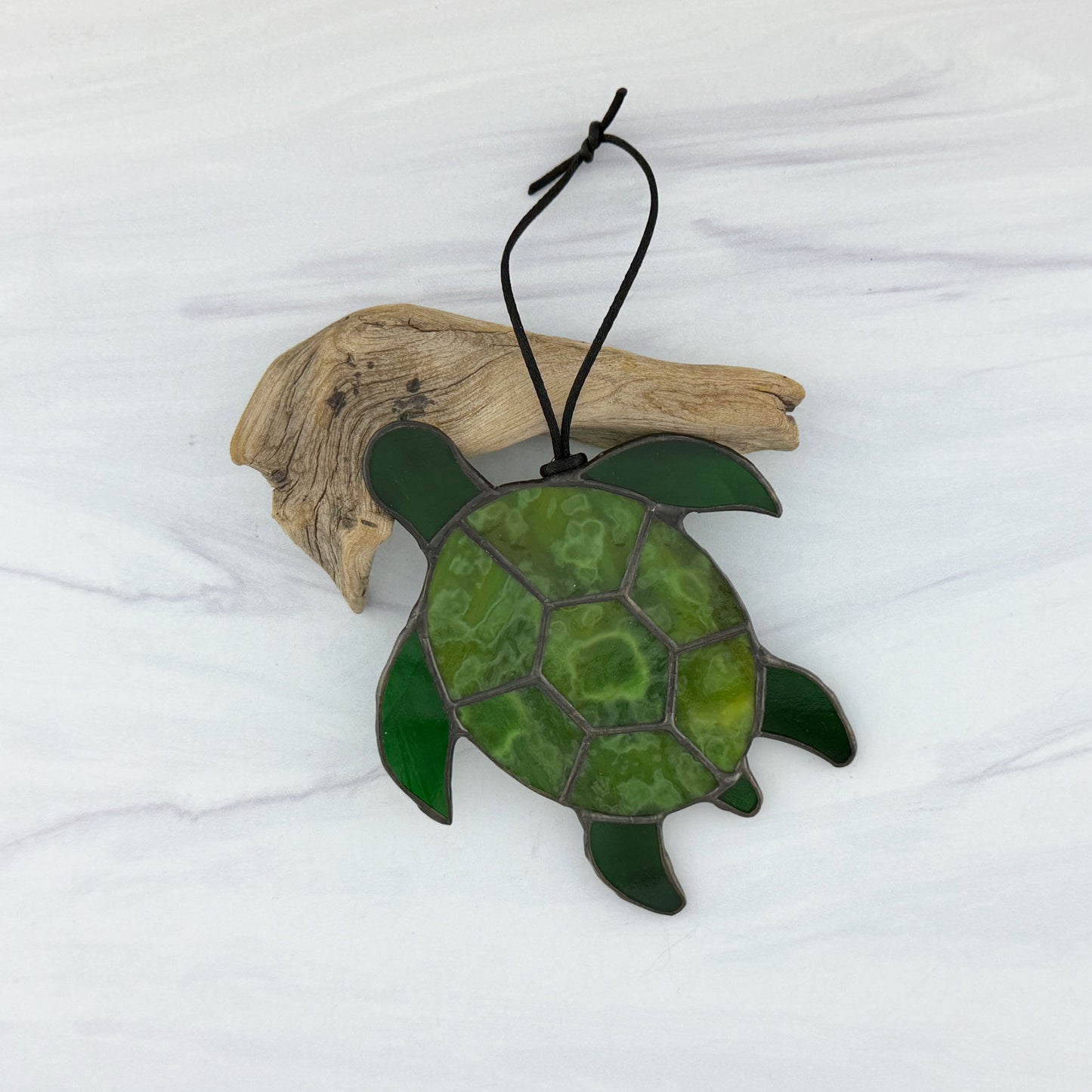 Stained glass mottled green sea turtle ornament resting on driftwood on a white background