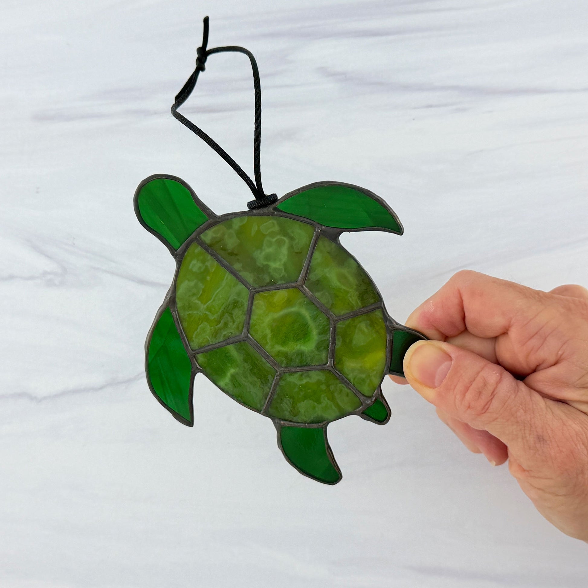 Hand holding a green stained glass turtle suncatcher against a white background
