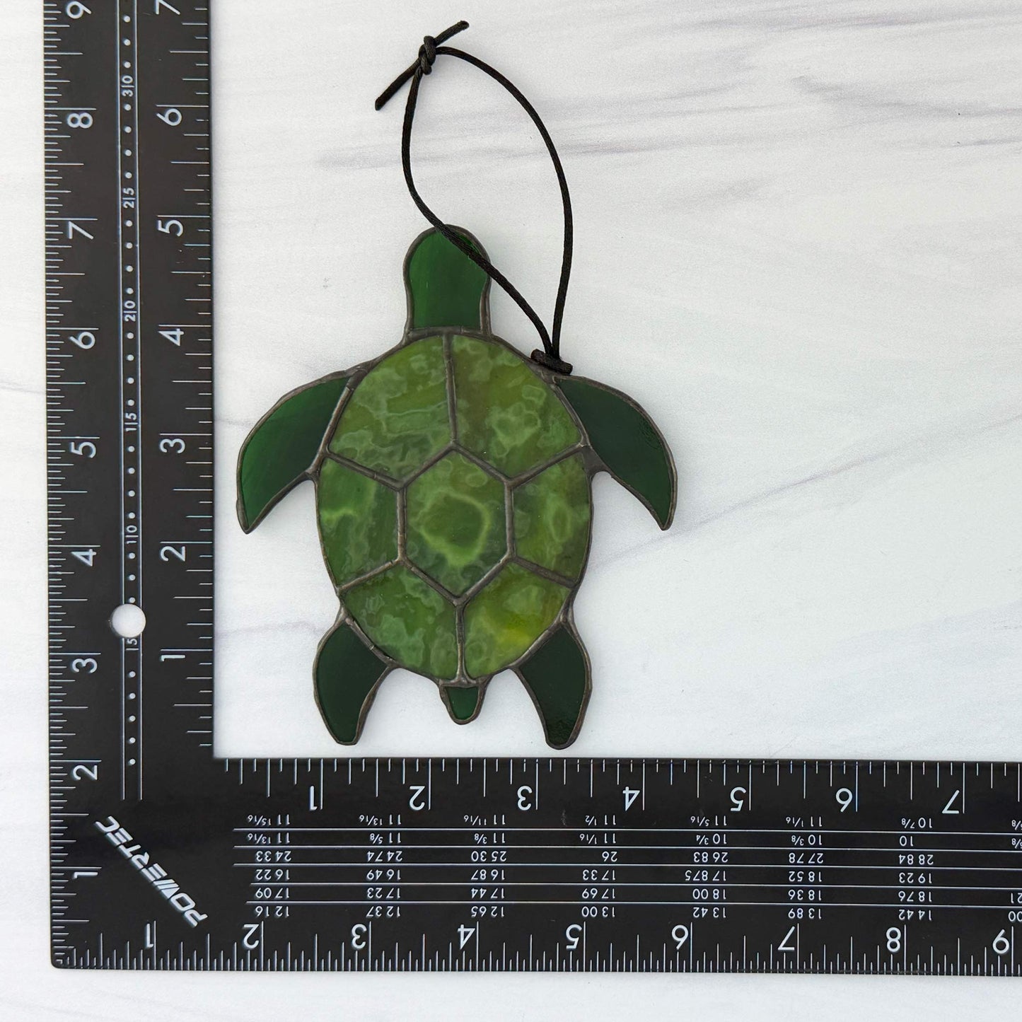 Green sea turtle suncatcher on a white background with a ruler for scale.