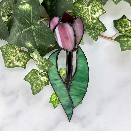 Stained glass tulip suncatcher.  The tulip is a striped pink and white with a red tip in the center. Swirling green glass is used for the two leaves and a dark green glass is used for the stem.  It measures 7.5 inches by 3 inches.stem